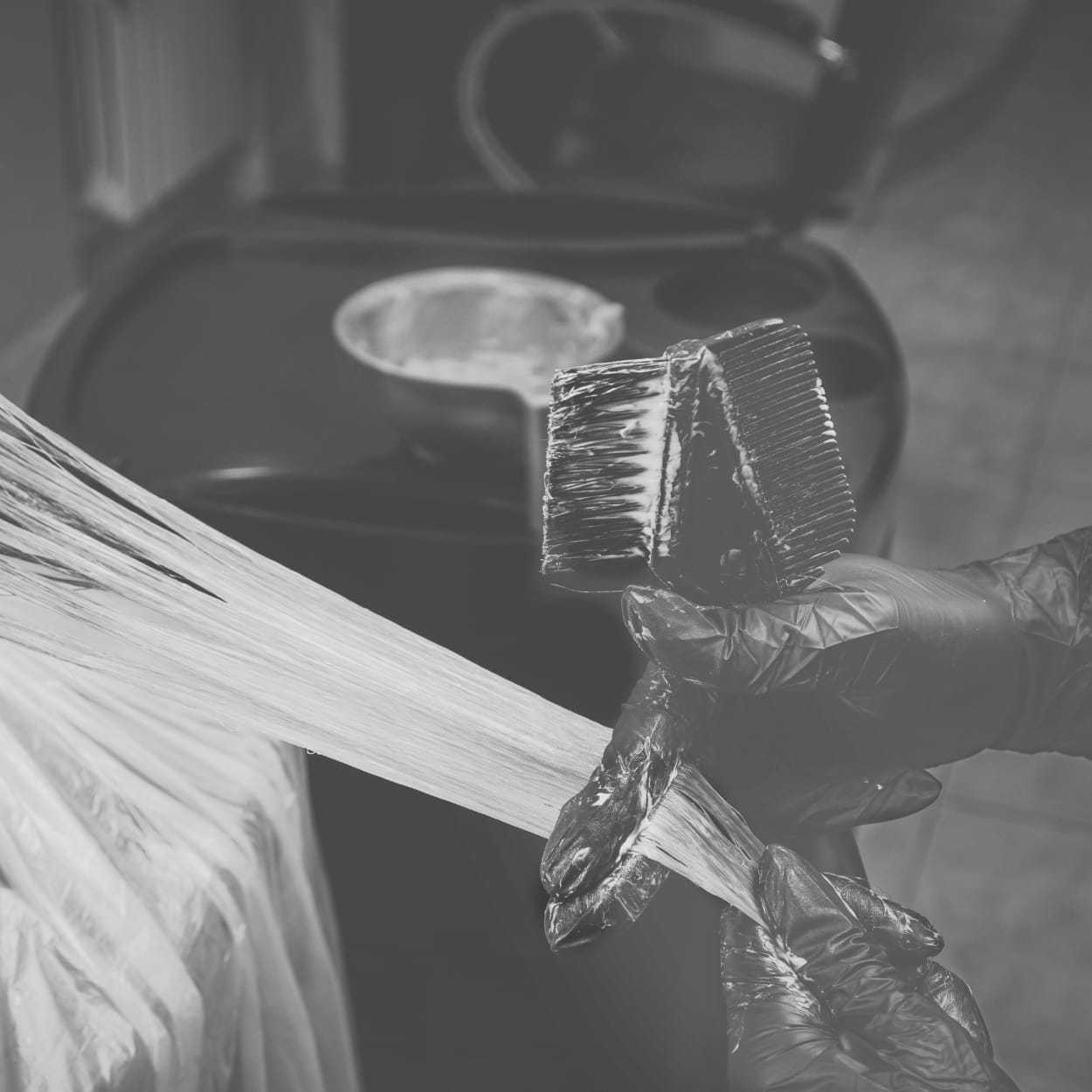 Hairdresser applying dye with a brush, gloved hands holding hair sections.
