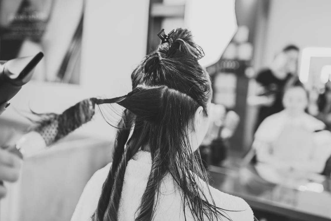 Person getting their hair styled in a salon, seen from behind with hair sectioned and twisted.