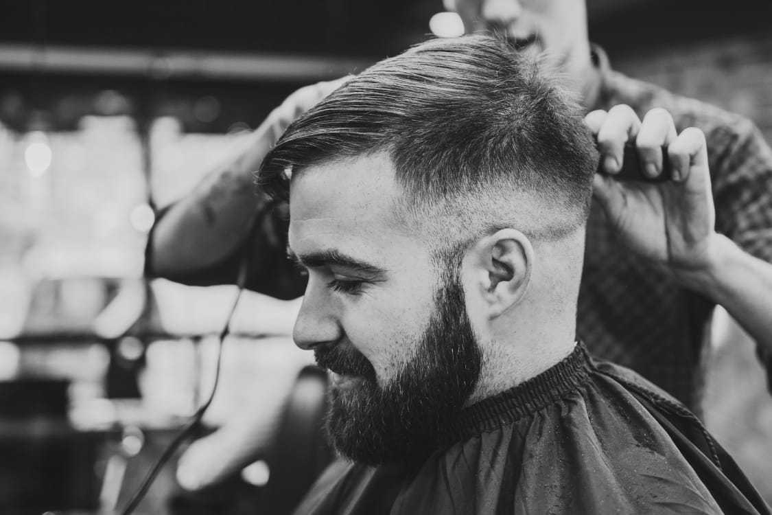 Man receiving a haircut at a barbershop, barber using clippers on the sides of his head.