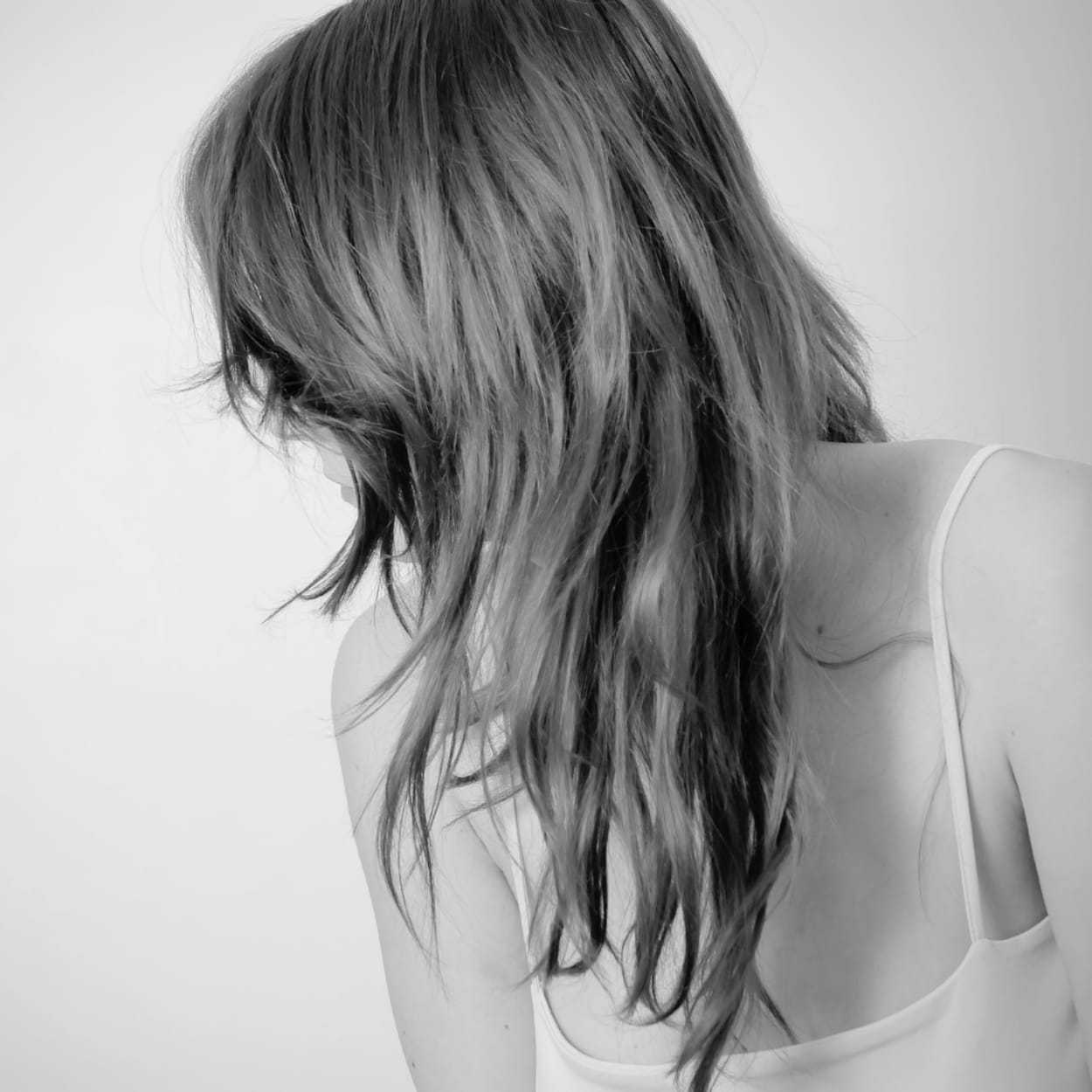 Woman with long, wavy hair facing away in a strappy top, captured in black and white.