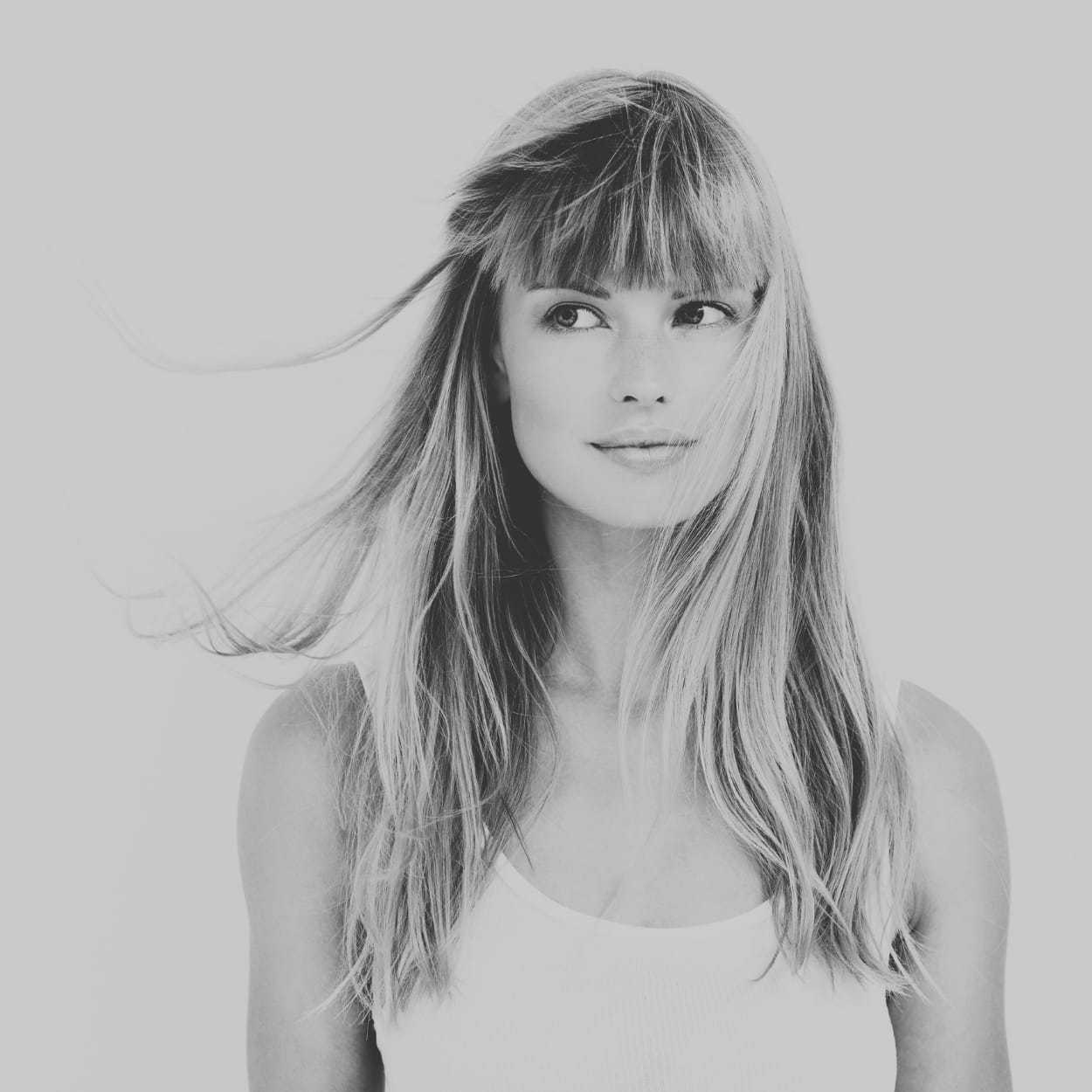 Black and white portrait of a smiling woman with long hair and bangs, looking to the side.