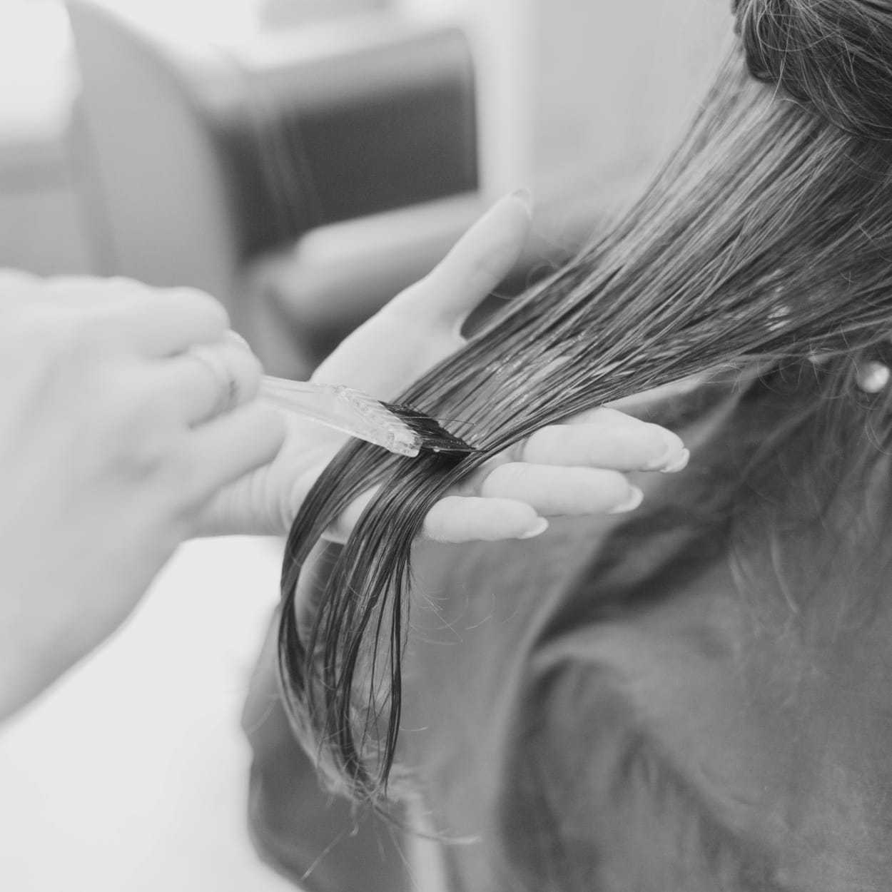 Hairdresser applying color to a woman's hair with a brush in a salon.