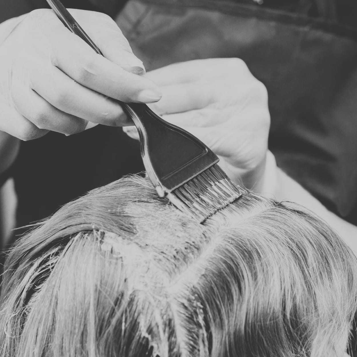 Hairdresser applying dye to client's hair roots with a brush.