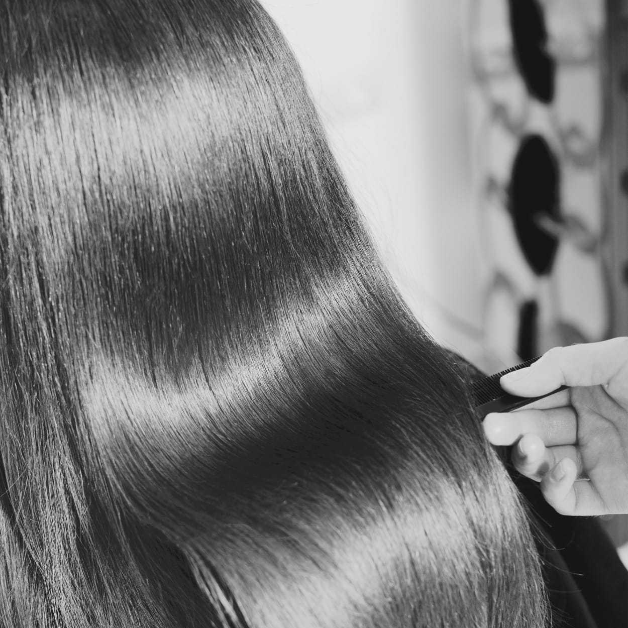 Close-up of shiny, straight hair being combed by a hand.