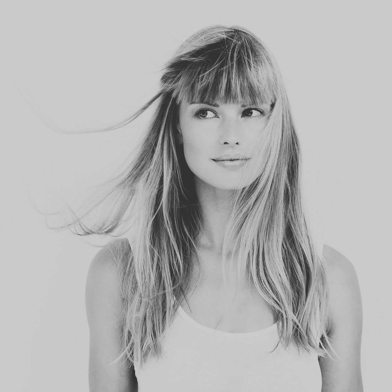 Black and white portrait of a smiling woman with long hair and bangs, looking to the side.