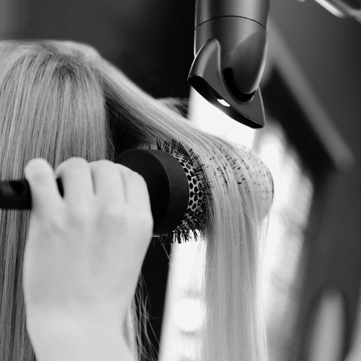 Hair being straightened with a round brush and hairdryer at a salon.