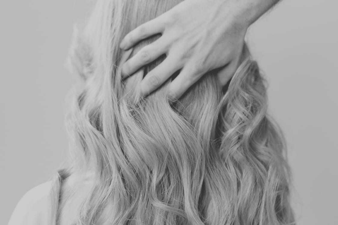Hand touching wavy blonde hair from behind, showcasing a soft hairstyle.