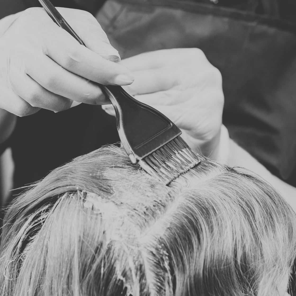 Hairdresser applying dye to client's hair roots with a brush.