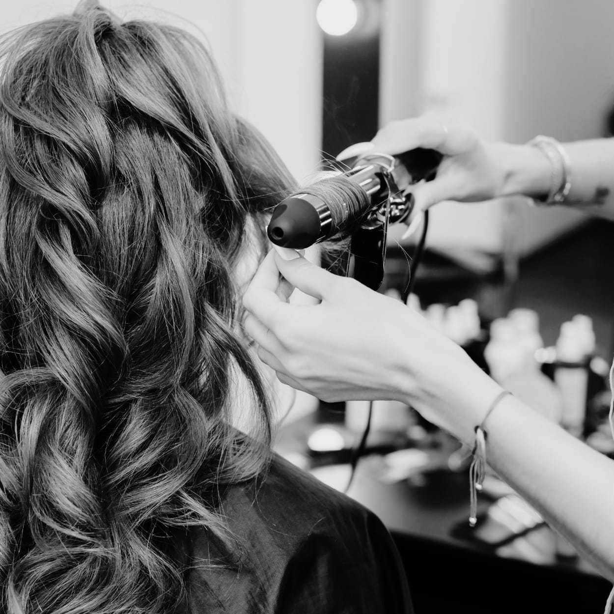 Person getting their hair styled with a curling iron in a salon.